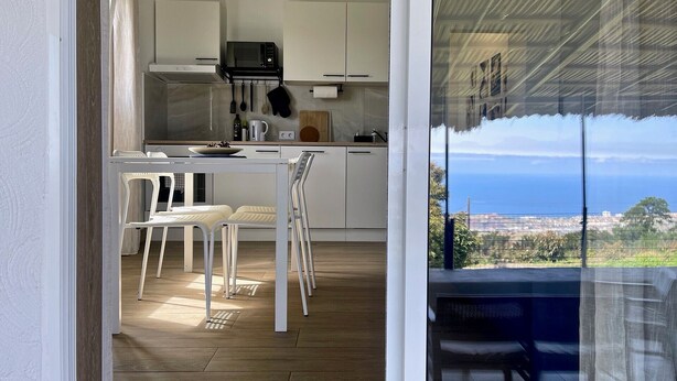 Una cocina moderna con gabinetes blancos, un microondas y una zona de comedor con sillas blancas.