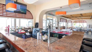 Una zona de bar con mostrador de granito, taburetes, una pantalla de televisión y lámparas colgantes naranjas.