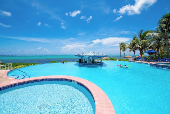A swimming pool with a view of the ocean, a lounge area with palm trees, and a covered seating area.