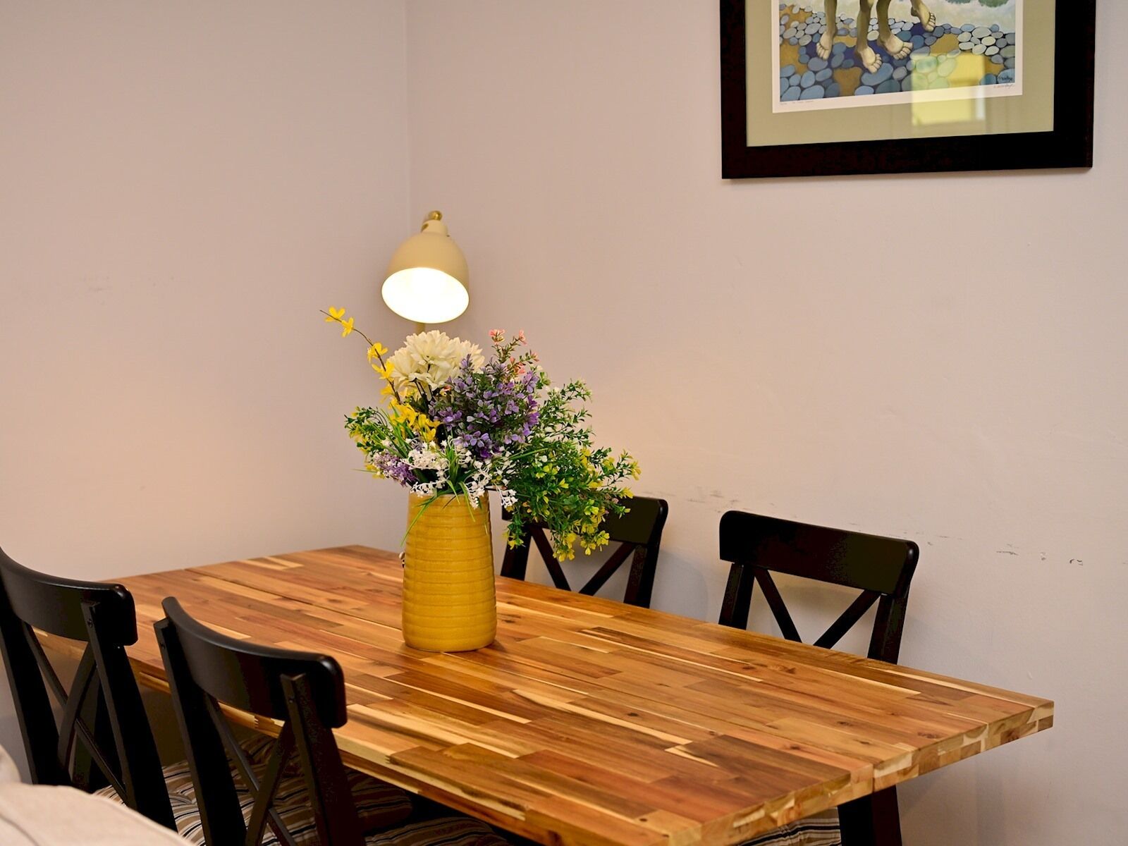 Ett matbord med en gul vas med blommor, en lampa och fyra stolar.