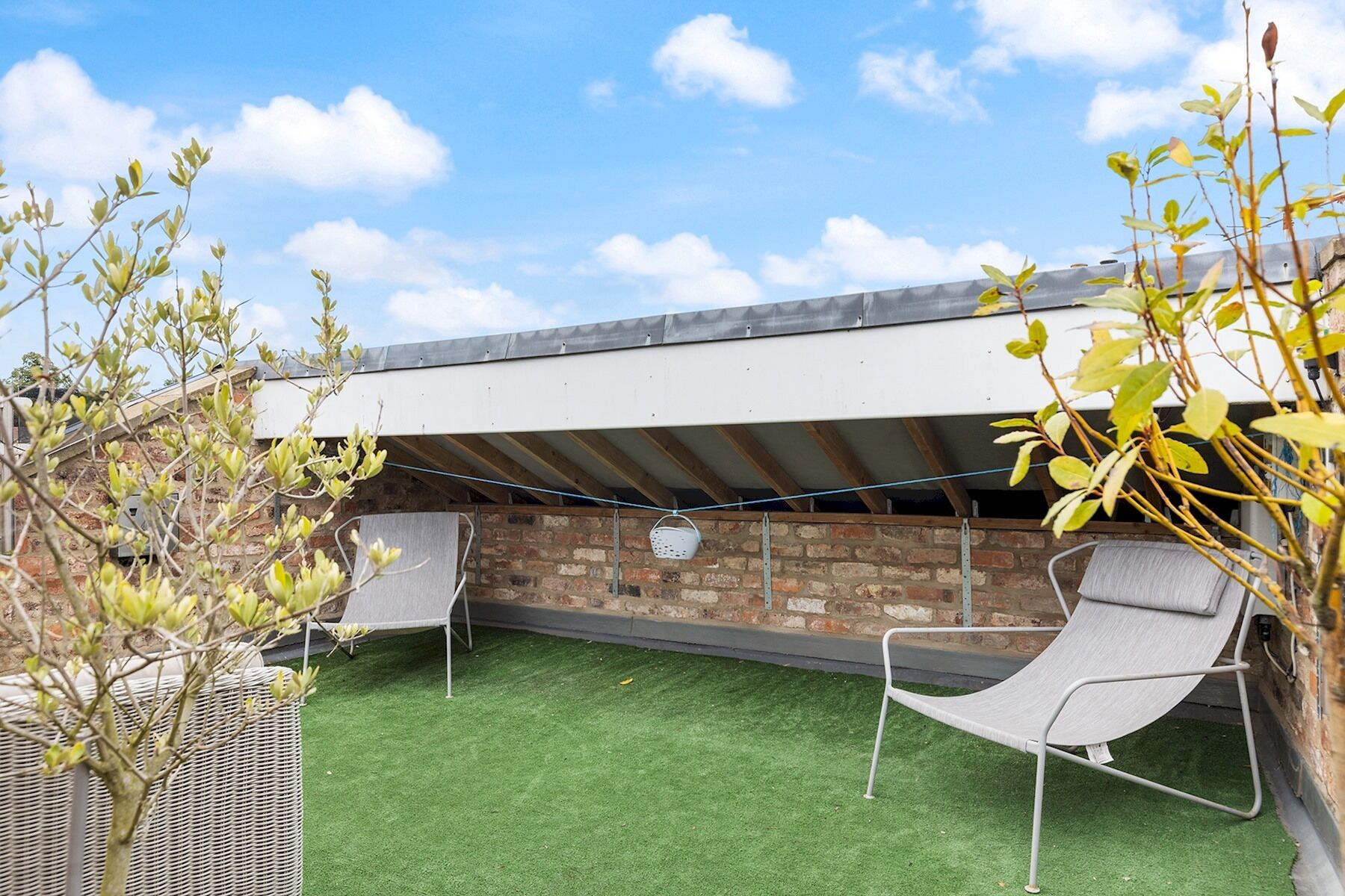 An outdoor patio with artificial grass, two metal chairs, a brick wall, and a metal roof structure.