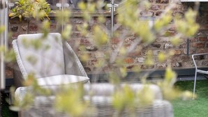 Une chaise en osier et une table dans un espace extérieur, avec un mur en briques et une pelouse artificielle.