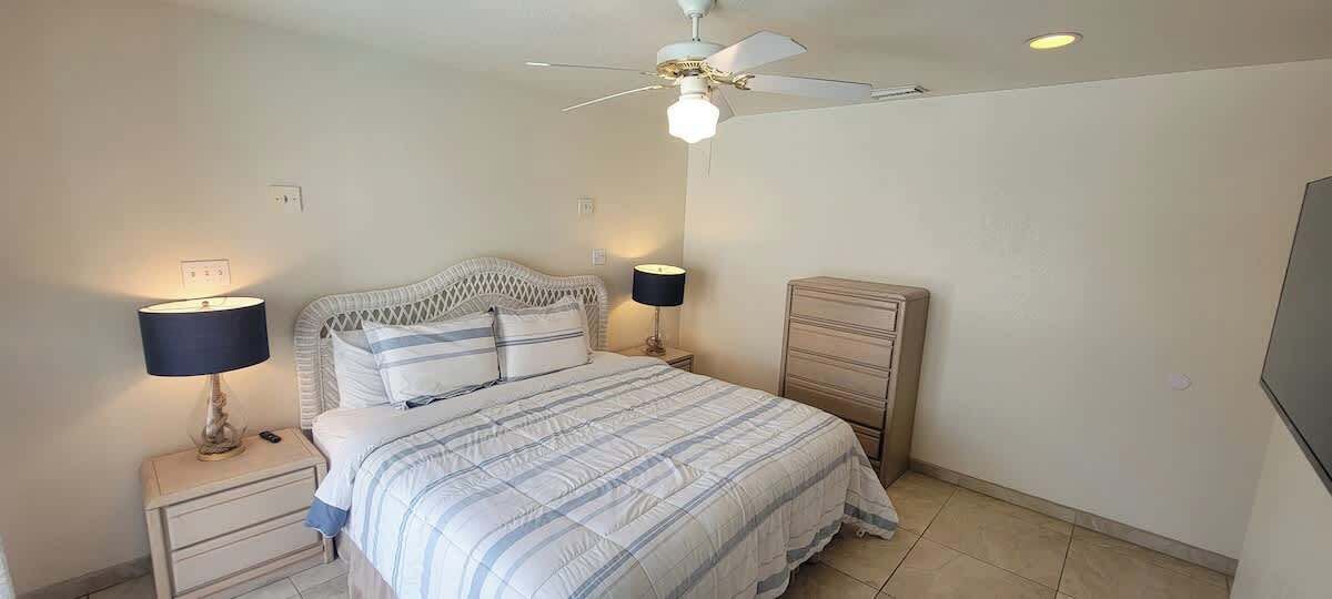A bedroom with a bed, two bedside tables with lamps, a ceiling fan, and a dresser.
