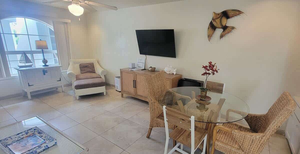 A living room with a glass table, wicker chairs, a white sofa, a television, and a decorative wall piece.