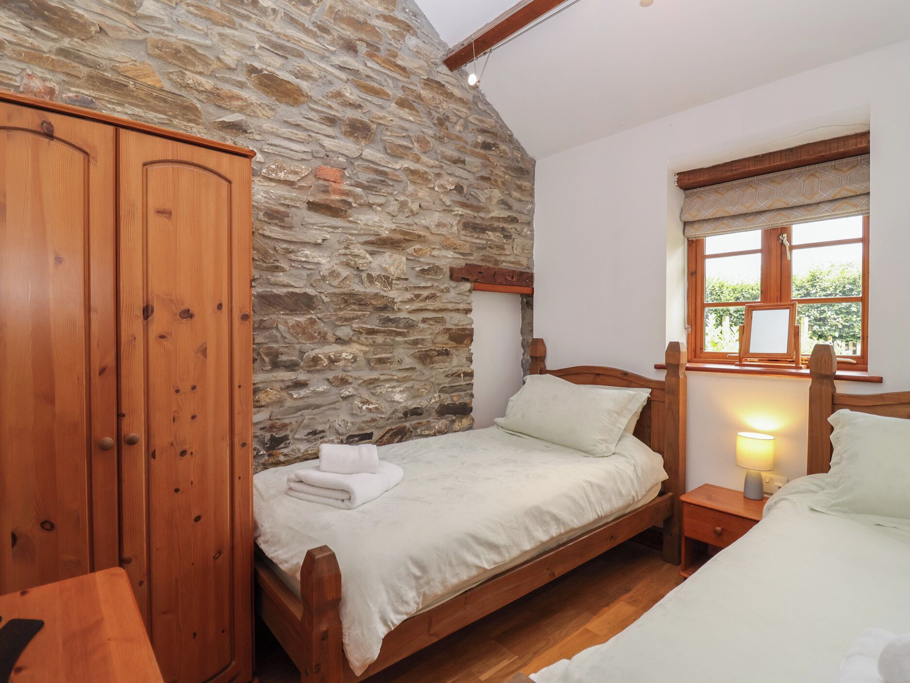 Une chambre à coucher avec un lit en bois, une table de chevet avec une lampe, une armoire et un mur en pierre.