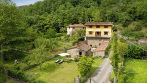 Une propriété située sur une colline, avec une maison jaune et un bâtiment en pierre, le tout entouré d’une végétation luxuriante.