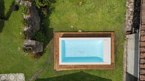 Vue aérienne d’une piscine rectangulaire dotée d’une terrasse en bois, entourée d’une pelouse verdoyante et d’un mur de pierres.
