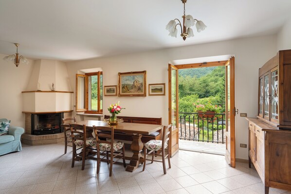 Un comedor con chimenea, una mesa de madera y sillas. Se aprecia un balcón con vistas a zonas verdes.