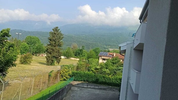 A balcony with a view of a green landscape, a clear sky, and distant mountains. - APARTMENT AVIANO (Aviano)