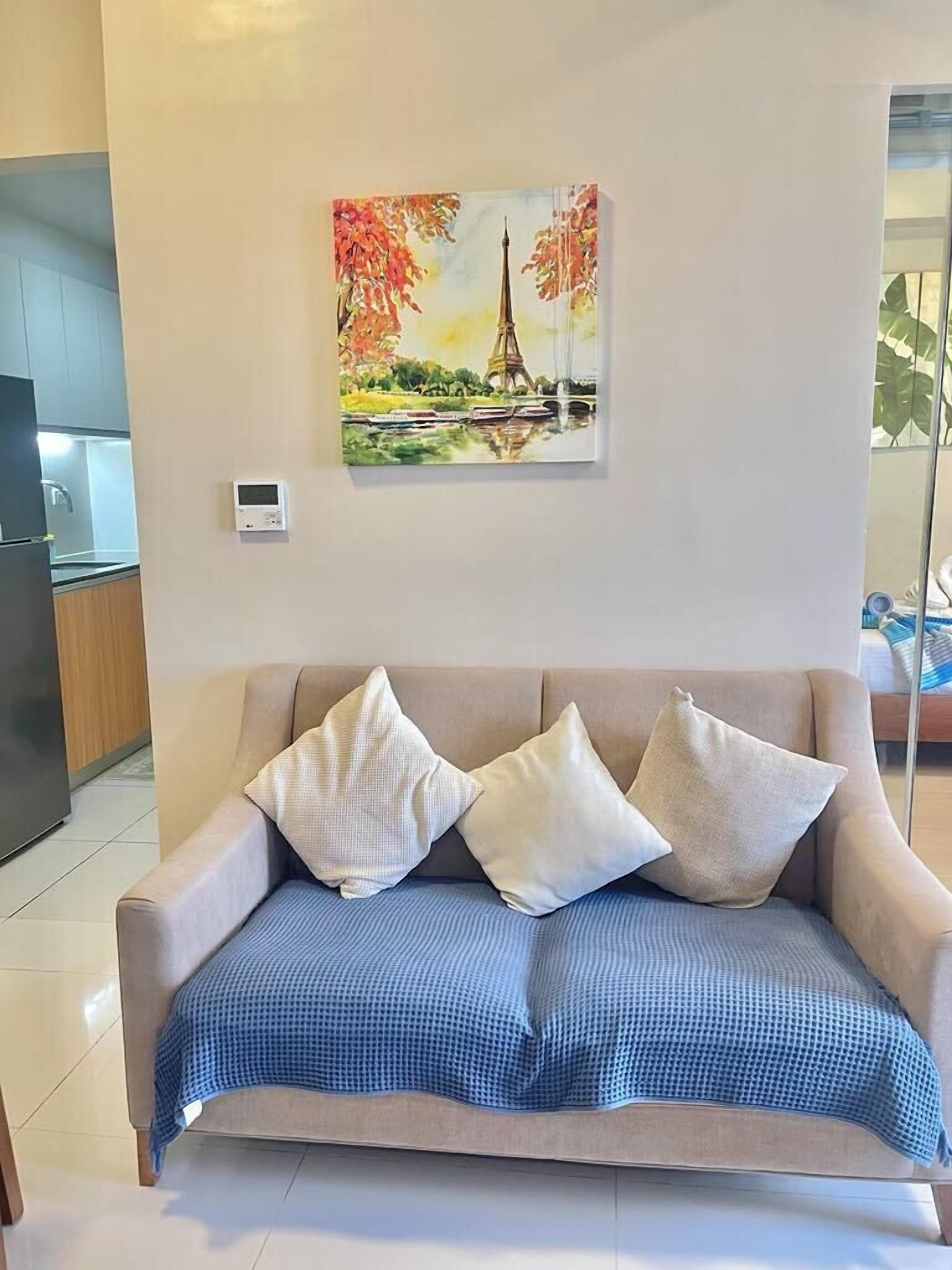 Een woonkamer met een beige bank, een blauw geruit plaid en een schilderij van de Eiffeltoren.