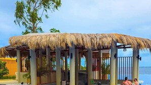 A poolside cabana with a thatched roof, surrounded by a clear blue pool. - MactanNewtown Staycation Near The Beach  (Lapu-Lapu)