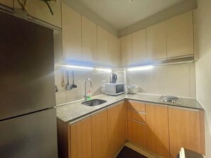 Eine kleine Küche mit Holzausstattung, einem Edelstahlkühlschrank, einer Mikrowelle und einem Spülbecken.