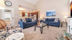 A spacious living room with two sofas, a coffee table, and a fireplace. A kitchen is visible in the background.
