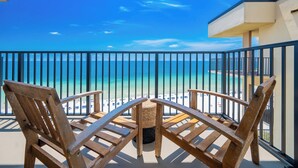 Een balkon met houten stoelen en een tafel, met uitzicht op een strand en een strakblauwe lucht.