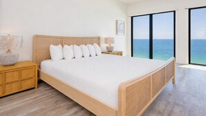 Een moderne slaapkamer met een groot bed, een houten hoofdbord, nachtkastjes en uitzicht op de oceaan.