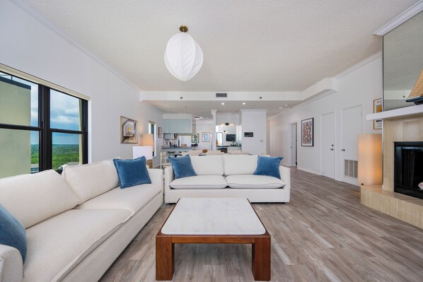 A spacious living room with a white sofa, a wooden coffee table, and a large window offering a view of the outdoors.