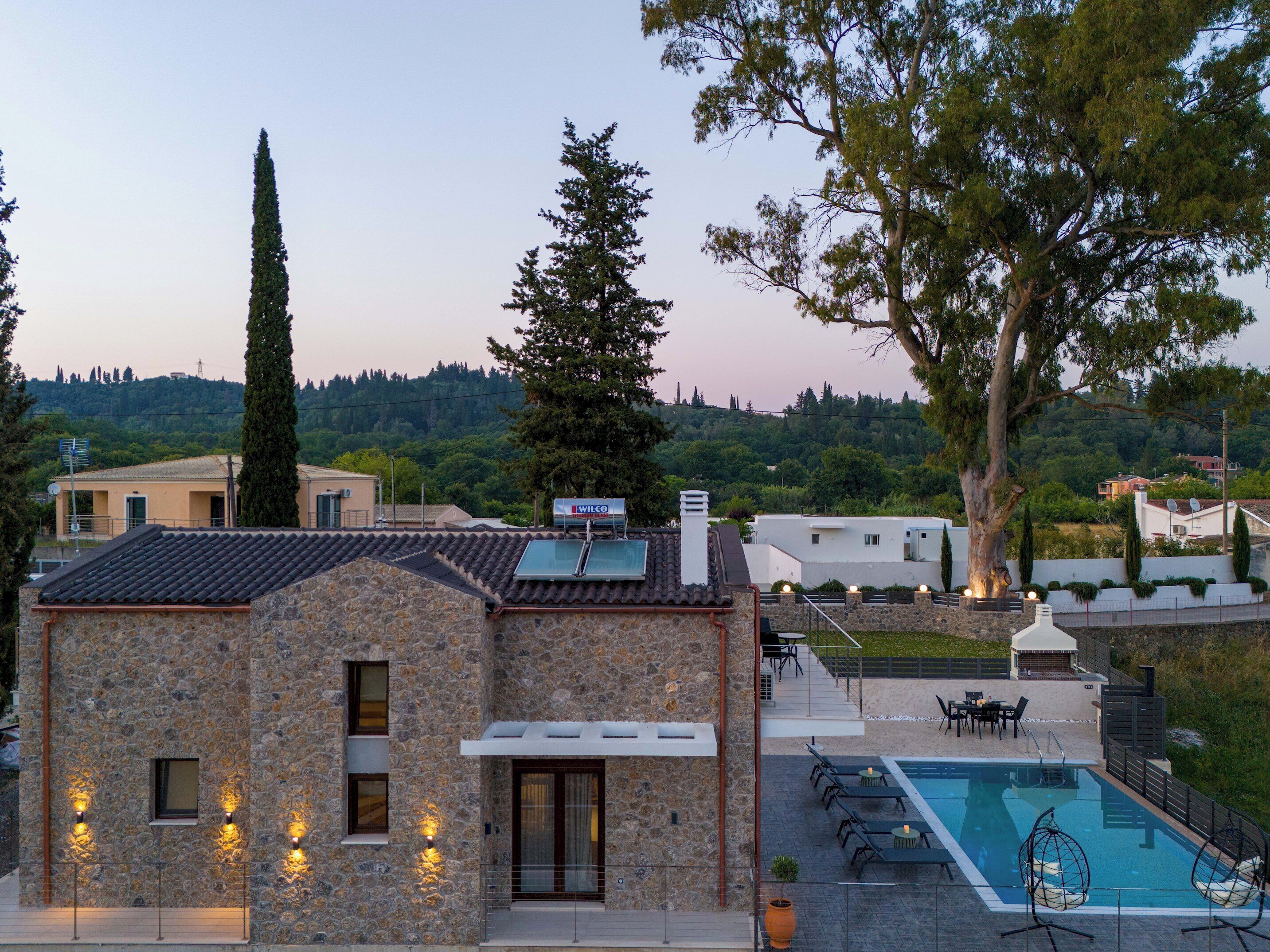 A stone building with a pool, outdoor seating, and a view of a hillside.