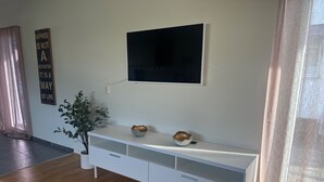 A modern living room with a white entertainment unit, a flat-screen TV mounted above it, and a potted plant beside the unit. - Modern 1-bedroom Apartment for 6 Near Kristianstad (Fjalkinge)