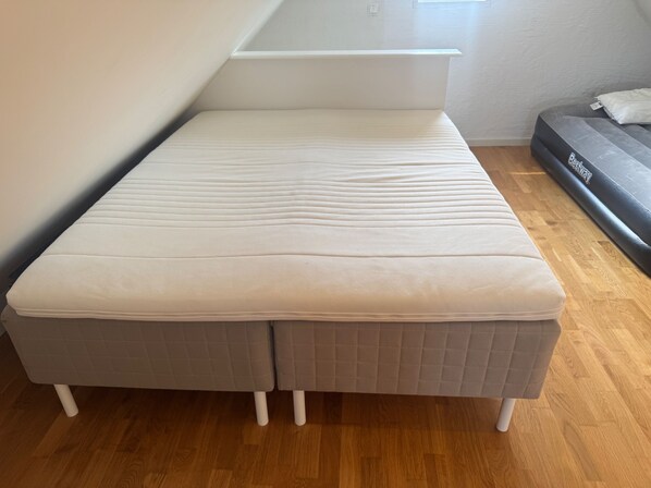 Quarto compacto com uma cama de solteiro, um pequeno sofá e uma janela que oferece luz natural.