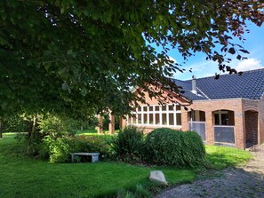 A brick building with large windows, a stone bench, and a grassy garden. - Villa in a cozy village in Southern Jutland (Tønder)