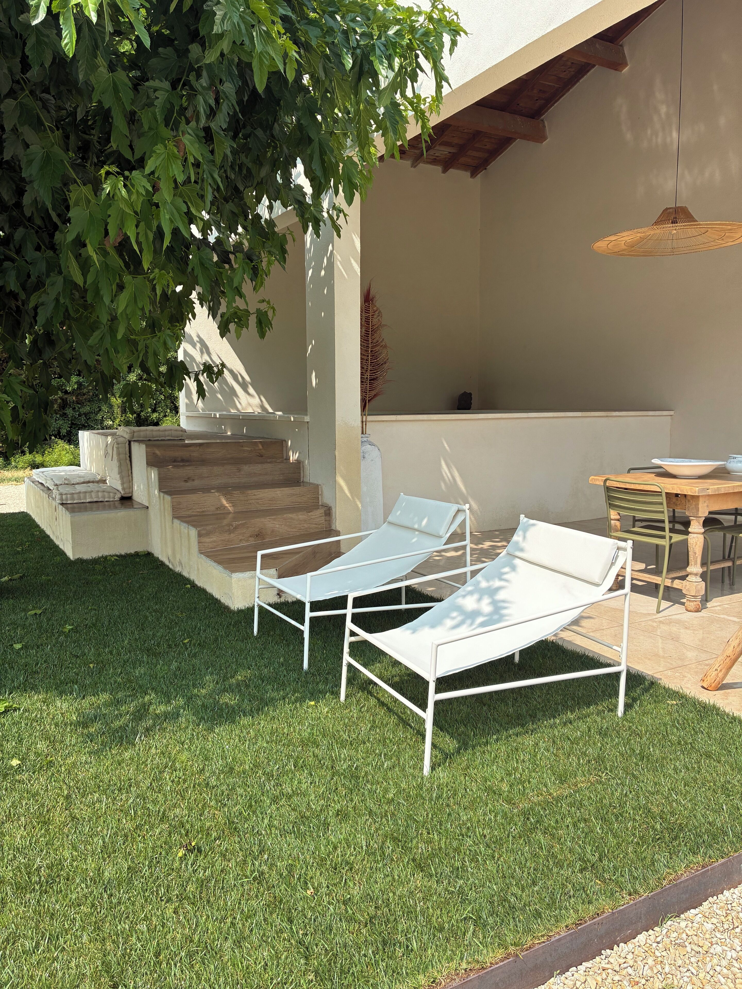 A patio area with a white lounge chair, a dining table with chairs, and a staircase leading to an upper level.