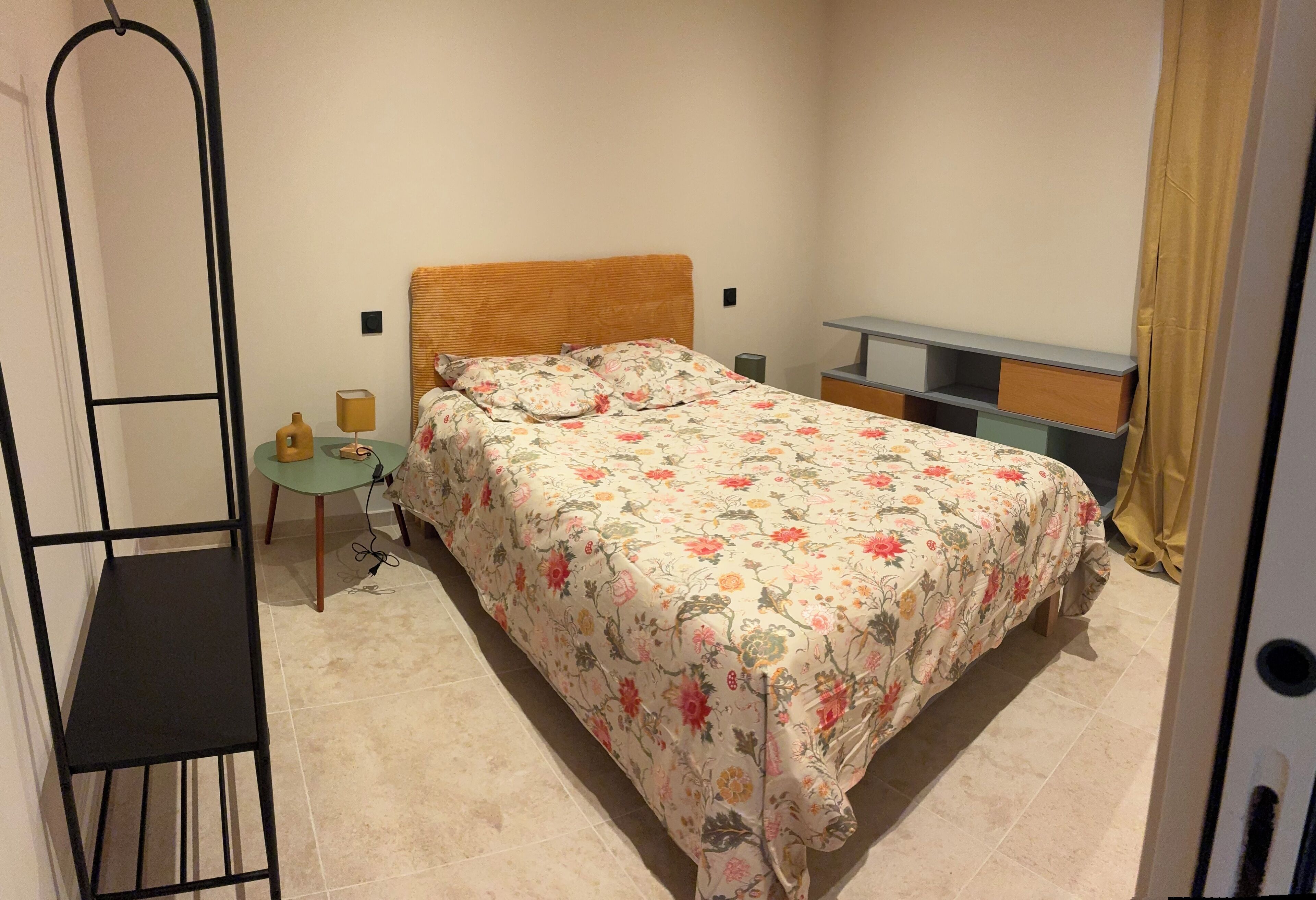 Une chambre à coucher comprenant un lit, une table de chevet, une petite table et une étagère.