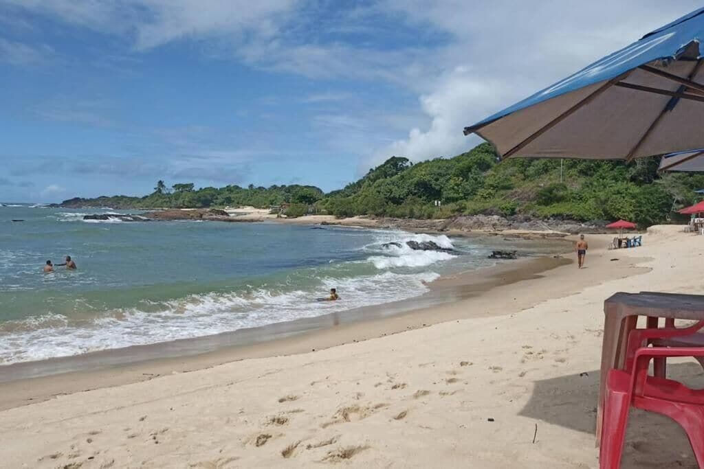 Una playa con orilla arenosa, algunas personas nadando y una silla roja en primer plano.