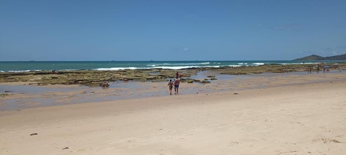 Una playa con gente caminando, una costa rocosa y el océano al fondo.