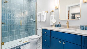 A modern bathroom with a glass shower enclosure, a white toilet, and a blue vanity with gold fixtures.