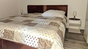 A neatly made bed with a patterned quilt, a wooden headboard, and a bedside table with a lamp.