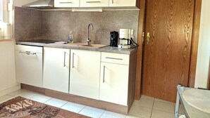 A compact kitchen with white cabinets, a stainless steel range hood, a coffee maker, and a wooden door.