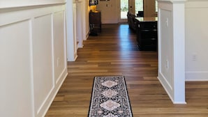 Un pasillo con suelo de madera, paneles blancos y un tapete con diseño blanco y negro.
