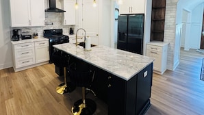 Una cocina moderna con armarios blancos, una isla de mármol e iluminación colgante.