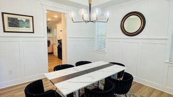 A dining area with a marble-top table, black chairs, a patterned rug, a chandelier, and a mirror on the wall.