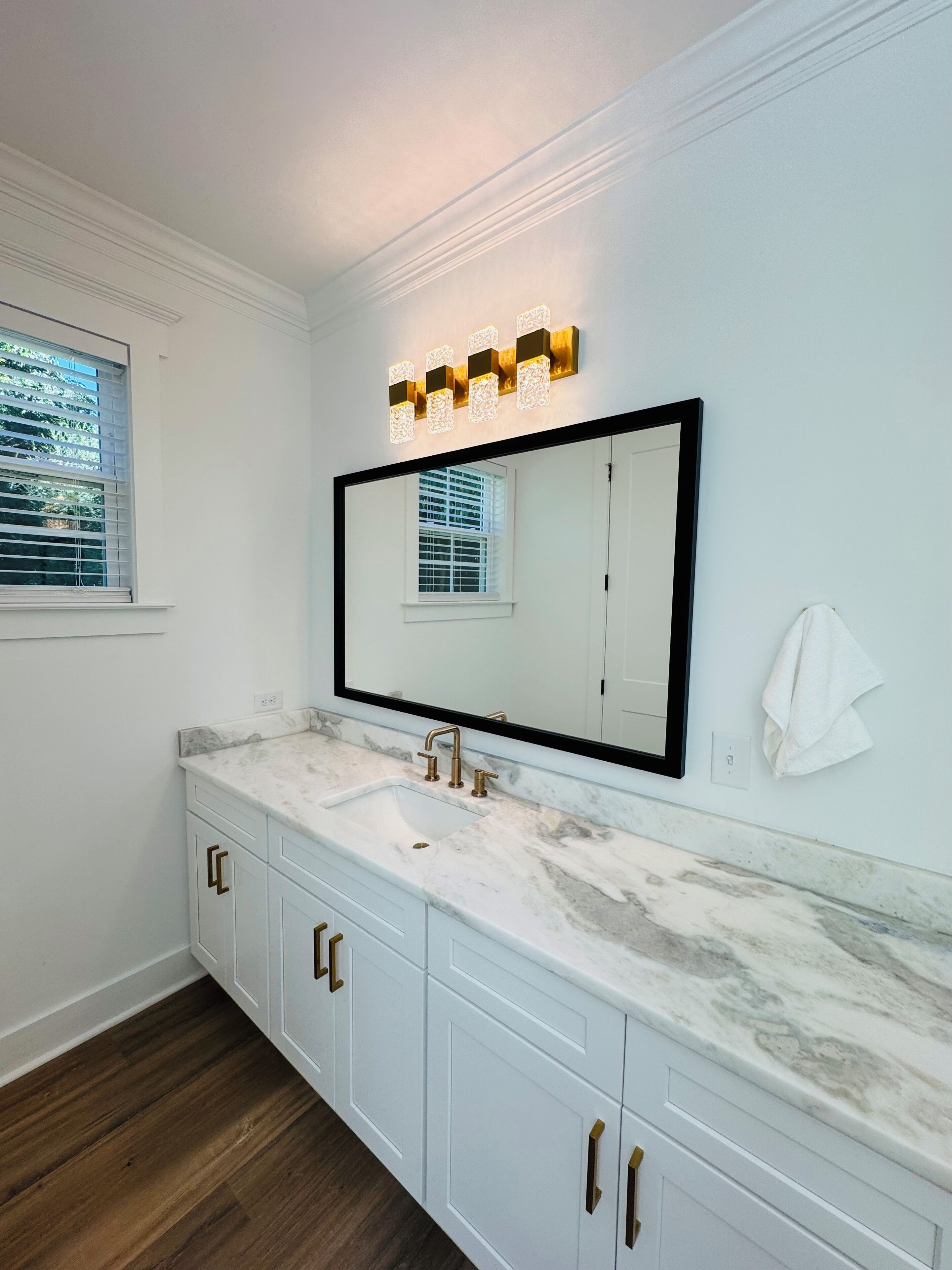 A bathroom with a large mirror, a sink with a marble countertop, and wooden flooring.
