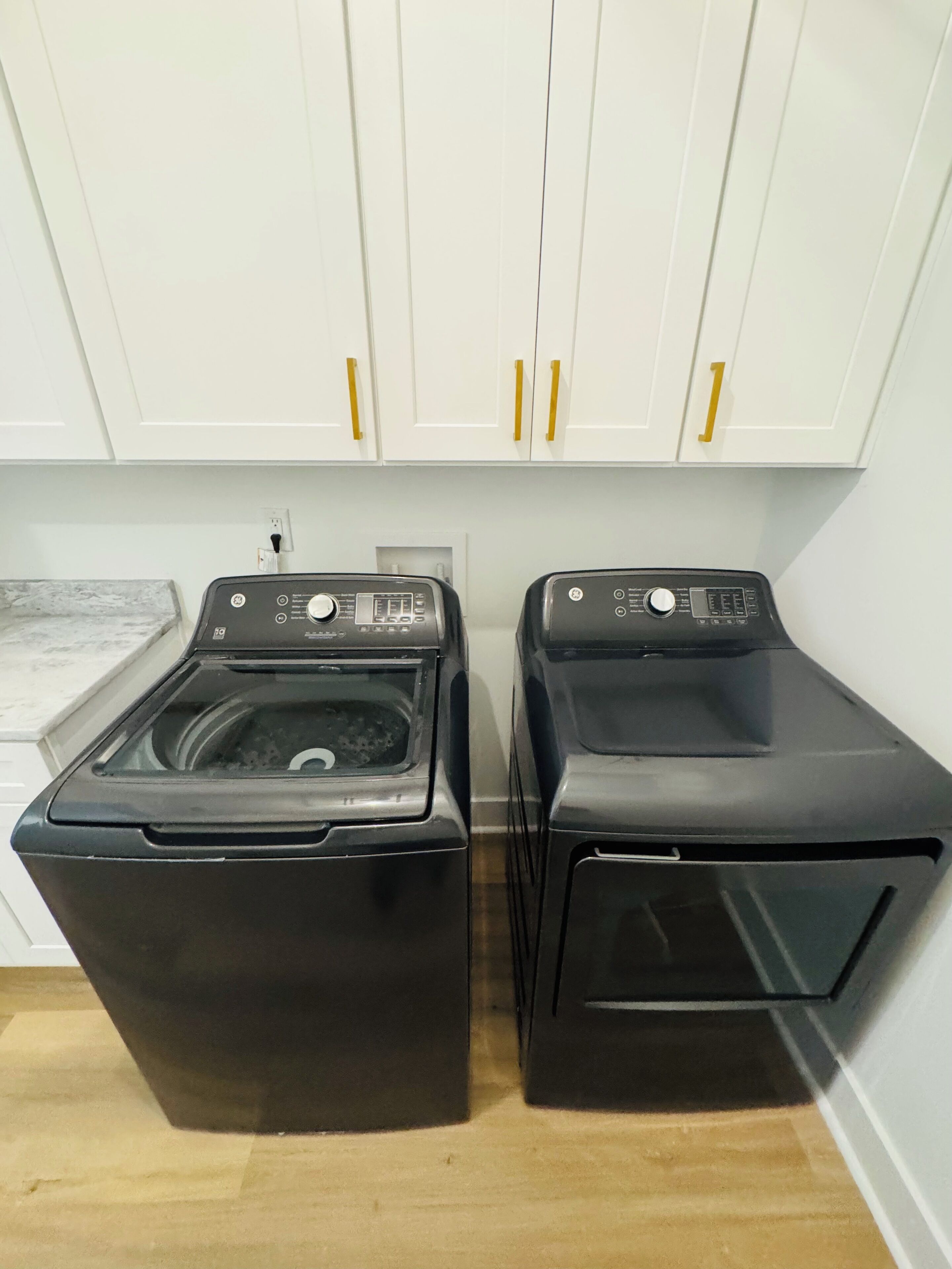 A laundry area with two front-loading washing machines and white cabinets with gold handles.