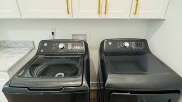 A laundry area with two front-loading washing machines and white cabinets with gold handles.
