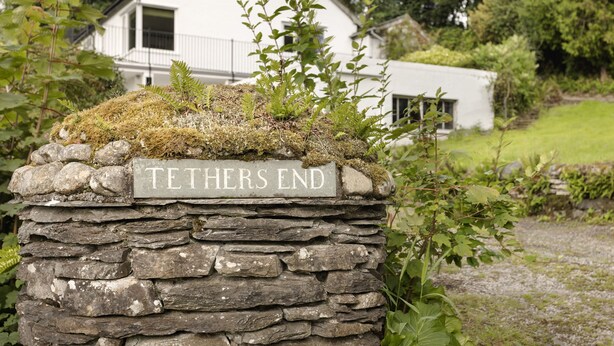 A stone sign with the inscription "TETHERS END" in a rural setting with a white house in the background. - Tethers End (Windermere)