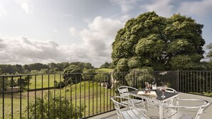 A balcony with a table and chairs, overlooking a grassy area and a large tree. - Tethers End (Windermere)