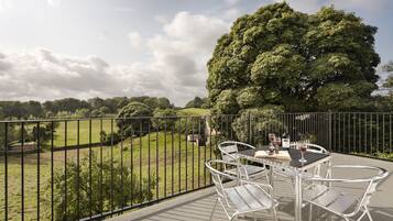 A balcony with a table and chairs, overlooking a grassy area and a large tree.