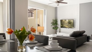 Un salon moderne avec un coin repas, comprenant un canapé, un téléviseur à écran plat fixé au mur et un ventilateur de plafond.