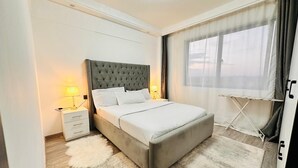 Ein ordentlich eingerichtetes Schlafzimmer mit einem großen Bett, Nachttischlampen, einem flauschigen Teppich und einem Fenster mit Vorhängen.