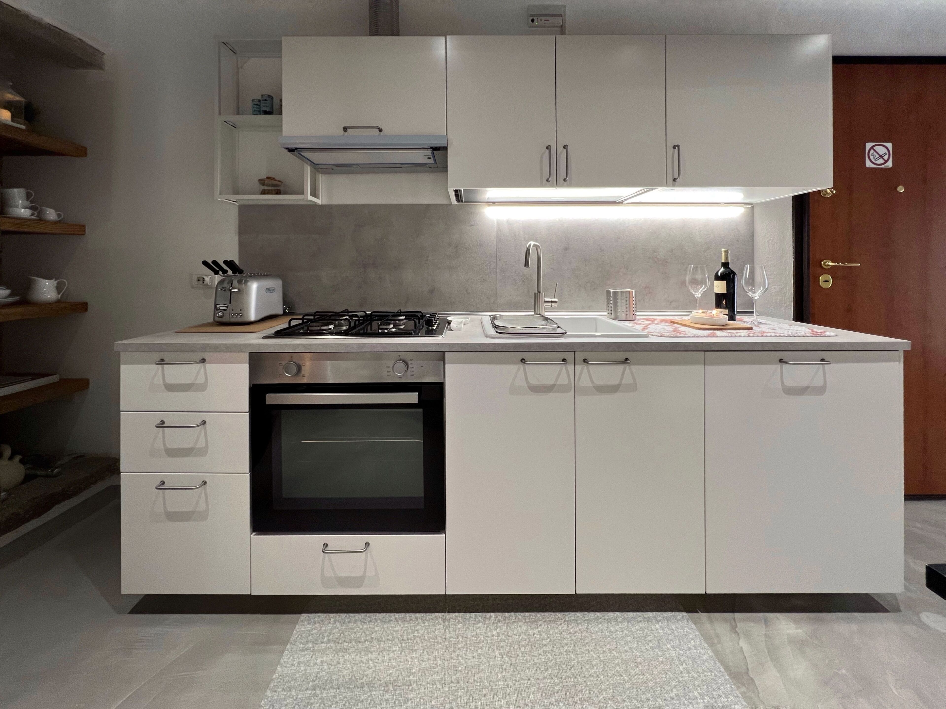 Een moderne keuken met witte kasten, een inbouwoven, een gasfornuis en een roestvrijstalen spoelbak.