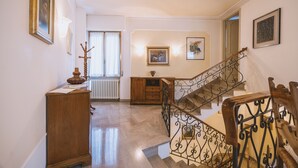 A spacious hallway with a wooden cabinet, a radiator, and a staircase with ornate metal railings. - CasAdòro - Two Bedroom Apartment, Sleeps 5 (Arezzo)
