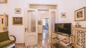 A room with a marble floor, a green sofa, a TV on a gold stand, and framed pictures on the walls. - CasAdòro - Two Bedroom Apartment, Sleeps 5 (Arezzo)