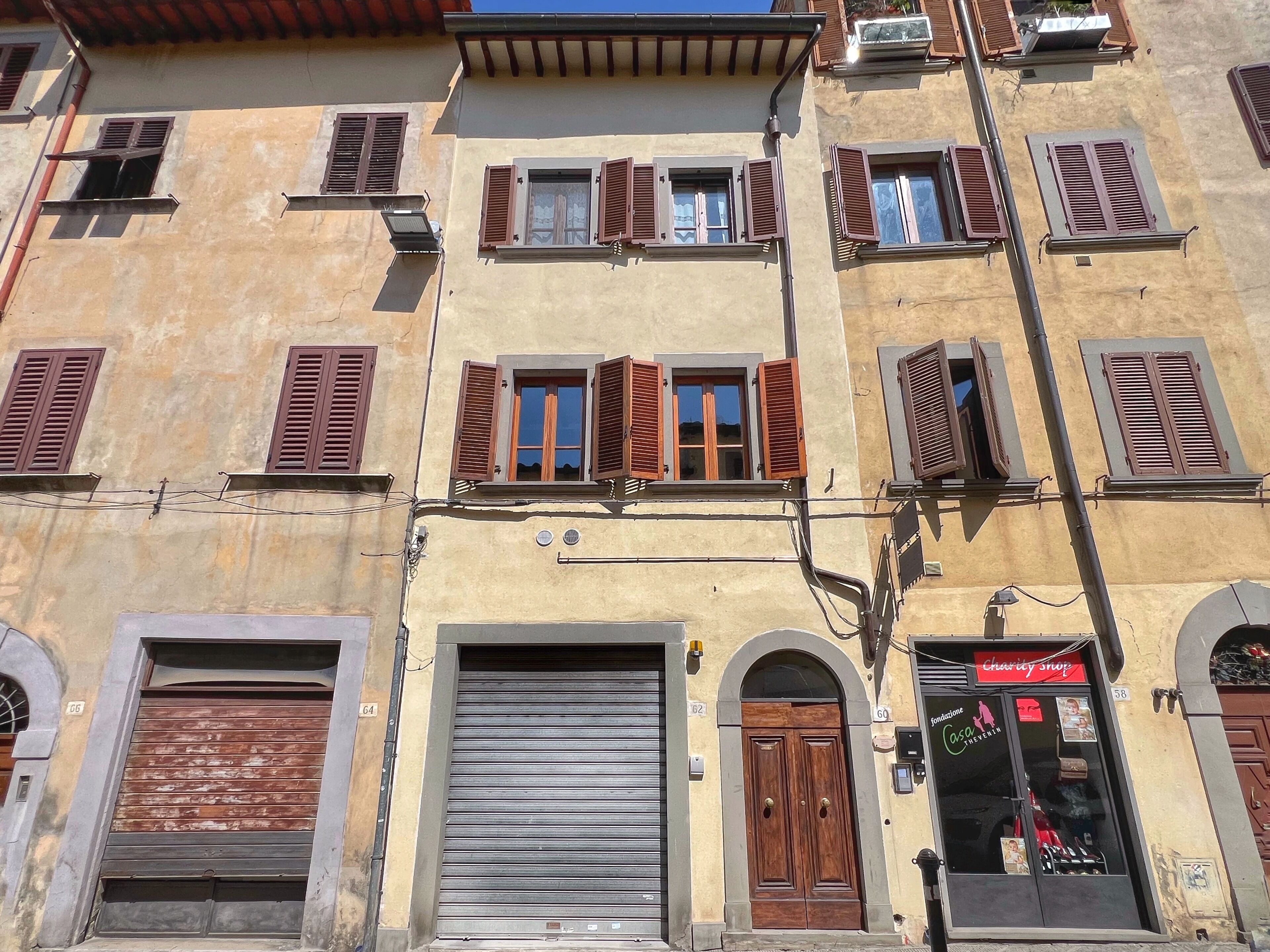 Un edificio con varias ventanas, algunas con contraventanas, una puerta metálica con persiana cerrada y una tienda con cartel.
