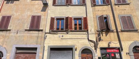 Un edificio con varias ventanas, algunas con contraventanas, una puerta metálica con persiana cerrada y una tienda con cartel.