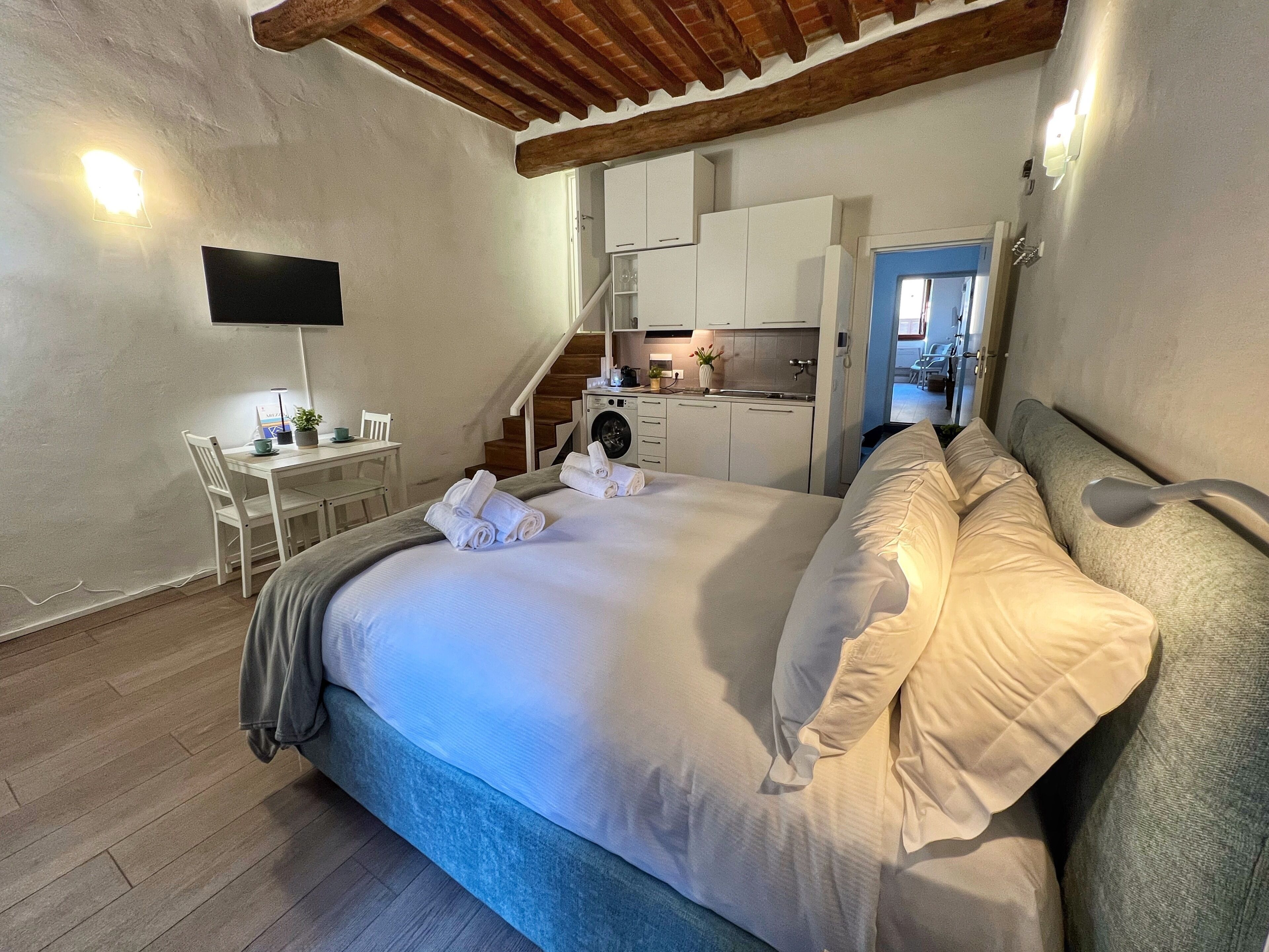 Un dormitorio con cama, escritorio, silla, televisor y una zona de cocina.