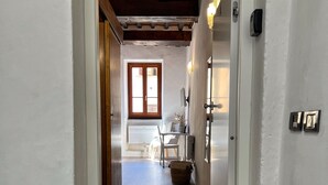 A hallway leading to a room with a wooden ceiling, a window, a door, and a small table with chairs.