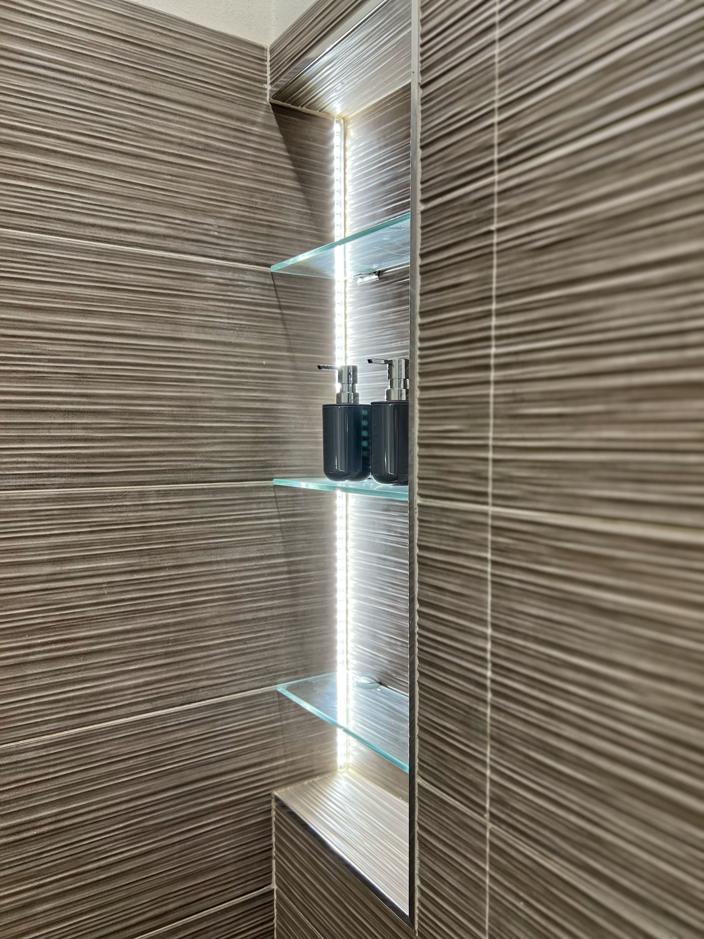A modern bathroom with a vertical mirror, a glass shelf with toiletries, and a textured wall.